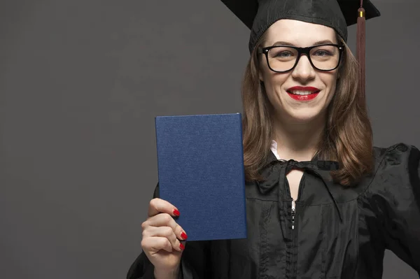 Charming female student smiling in eyeglasses wearing black mantle — Stock Photo, Image