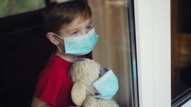Maskeli bir çocuk pencereden dışarı sallanıyor.