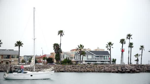 PORT HUENEME, CA U.S.A - JUNE 2015: Two men set sail out of harbor on overcast morning aboard sailboat. — ストック動画