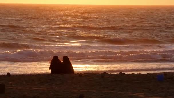 Duas fêmeas sentadas na praia ao pôr do sol — Vídeo de Stock