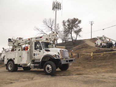 VENTURA, USA - JANUARY 5, 2018: repair trucks and crews on hill near damaged telephone lines form Thomas Fire  clipart