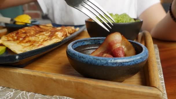 Birisi restoranda domuz pastırması, omlet, salata ve avokado yiyor. Bir tabakta çırpılmış yumurta. Lezzetli. Yakın plan — Stok video
