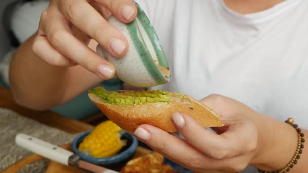 Mädchen gießt Sesamsoße auf eine Bruschetta mit Avocado. Frühstück. Gesunde Ernährung. Veganes Essen. Nahaufnahme — Stockvideo