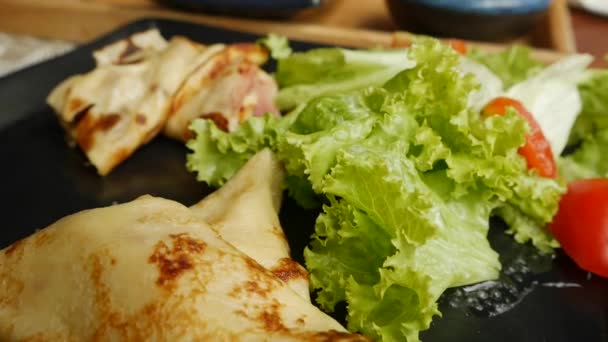 Pfannkuchen mit Schinken und Käse auf einem schwarzen Teller mit Salat in einem Restaurant. Frühstück. Nahaufnahme — Stockvideo