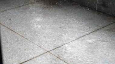 Yakından, büyük, yoğun yağmur damlaları püskürterek düşüyor. Yere su sıçrıyor. Balkondaki yağmurdan büyük damlalar.