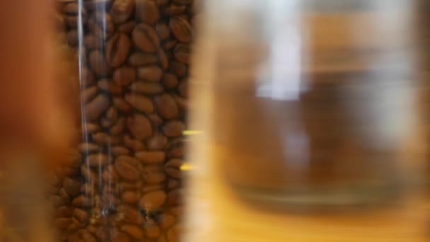 Muchas variedades de granos de café en frascos de vidrio en una mesa de madera en un café. Primer plano — Vídeo de stock