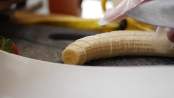 Close-up mãos de chef em luvas cortando uma banana com faca para fazer sobremesa ou purê — Vídeo de Stock