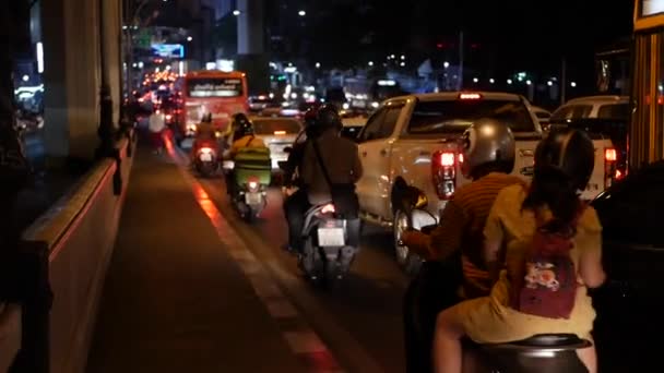 Auto e motobikes nel traffico di notte in città. La gente cammina sul marciapiede. BANGKOK, THAILANDIA - 01 DICEMBRE 2019 — Video Stock