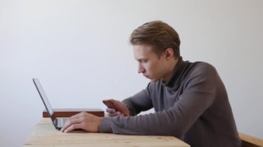 Yakışıklı genç adam dizüstü bilgisayar ve akıllı telefon kullanıyor, bir mesaj yazıyor, sohbet ediyor, telefonda bilgi arıyor. Yakın plan. 4k