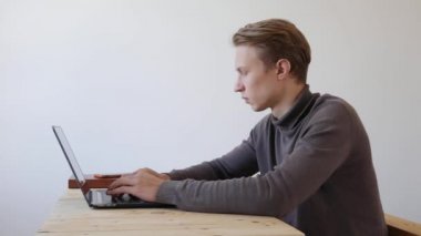 Yakışıklı genç adam dizüstü bilgisayar ve akıllı telefon kullanıyor, bir mesaj yazıyor, sohbet ediyor, telefonda bilgi arıyor. Yakın plan. 4k