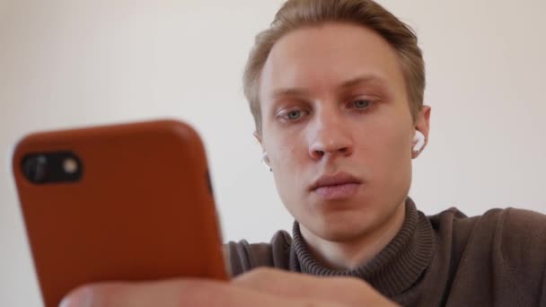 Handsome jongeman maakt gebruik van een smartphone, schrijft een bericht, chatten, op zoek naar informatie in de telefoon. Close-up — Stockvideo