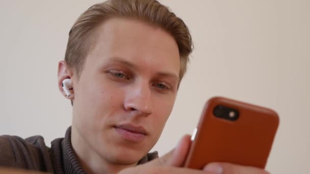 Glücklich aussehender junger Mann benutzt ein Smartphone, schreibt eine Nachricht, chattet, sucht nach Informationen im Telefon. Nahaufnahme — Stockvideo