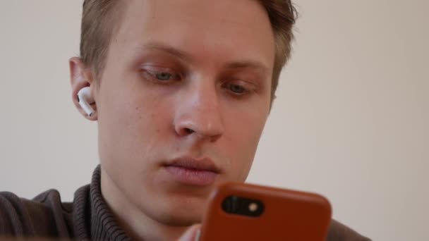 Όμορφος νεαρός χρησιμοποιεί ένα smartphone, γράφει ένα μήνυμα, συνομιλεί, ψάχνει για πληροφορίες στο τηλέφωνο. Κοντινό πλάνο — Αρχείο Βίντεο
