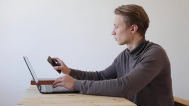 Yakışıklı genç adam dizüstü bilgisayar ve akıllı telefon kullanıyor, bir mesaj yazıyor, sohbet ediyor, telefonda bilgi arıyor. Yakın plan. 4k