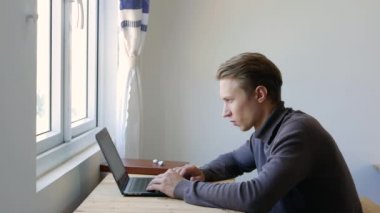Genç adam dizüstü bilgisayar kullanıyor, daktilo ediyor, kaydırıyor, internette sörf yapıyor, ekrana bakıyor. Profesyonel yaratıcı milenyum, ofis stüdyosundaki masasında çalışıyor. Öğrenci çevrimiçi çalışıyor. 4k
