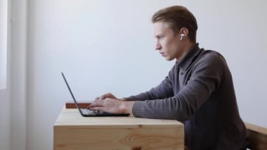 Genç adam dizüstü bilgisayar kullanıyor, daktilo ediyor, kaydırıyor, internette sörf yapıyor, ekrana bakıyor. Profesyonel yaratıcı milenyum, ofis stüdyosundaki masasında çalışıyor. Öğrenci çevrimiçi çalışıyor. 4k