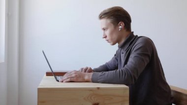 Genç yakışıklı adam dizüstü bilgisayar kullanıyor, kayıyor, internette sörf yapıyor, ekrana bakıyor. Profesyonel yaratıcı milenyum, ofis stüdyosundaki masasında çalışıyor. Öğrenci çevrimiçi çalışıyor. 4k