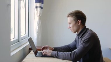 Genç adam dizüstü bilgisayar kullanıyor, daktilo ediyor, kaydırıyor, internette sörf yapıyor, ekrana bakıyor. Profesyonel yaratıcı milenyum, ofis stüdyosundaki masasında çalışıyor. Öğrenci çevrimiçi çalışıyor. 4k