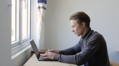 Genç adam dizüstü bilgisayar kullanıyor, daktilo ediyor, kaydırıyor, internette sörf yapıyor, ekrana bakıyor. Profesyonel yaratıcı milenyum, ofis stüdyosundaki masasında çalışıyor. Öğrenci çevrimiçi çalışıyor. 4k