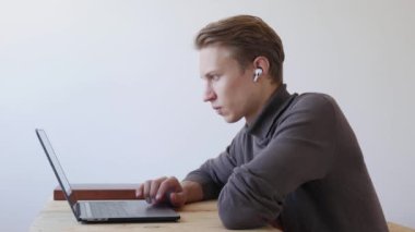 Genç yakışıklı adam dizüstü bilgisayar kullanıyor, kayıyor, internette sörf yapıyor, ekrana bakıyor. Profesyonel yaratıcı milenyum, ofis stüdyosundaki masasında çalışıyor. Öğrenci çevrimiçi çalışıyor. 4k