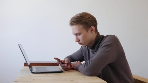 Schöner junger Mann benutzt Laptop und Smartphone, schreibt eine Nachricht, chattet, sucht nach Informationen im Telefon. Nahaufnahme. 4k — Stockvideo