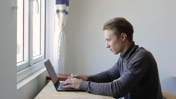 Junger Freiberufler mit Laptop, Tippen, Scrollen, Surfen im Internet, Blick auf den Bildschirm. Professionelle kreative Millennials arbeiten an seinem Schreibtisch im Homeoffice-Studio. Studenten studieren online. 4k — Stockvideo