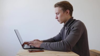 Genç adam dizüstü bilgisayar kullanıyor ve telefonda konuşuyor. Profesyonel yaratıcı milenyum, ofis stüdyosundaki masasında çalışıyor. Öğrenci çevrimiçi çalışıyor. 4k