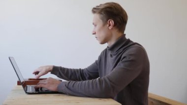 Genç adam dizüstü bilgisayar kullanıyor ve telefonda konuşuyor. Profesyonel yaratıcı milenyum, ofis stüdyosundaki masasında çalışıyor. Öğrenci çevrimiçi çalışıyor. 4k