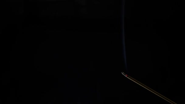 Крупный план горящей благовонной палочки. Дым дует с конца горячего угля. Запах, выпущенный из ладана на черном фоне. Расслабление, медитация и ароматерапия. 4k — стоковое видео