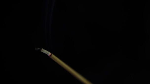 Detailní pohled na hořící vonnou tyčinku. Kouř fouká z konce žhavého září. Vůně uvolněná z kadidla na černém pozadí. Relaxace, meditace a aromaterapie. 4k — Stock video