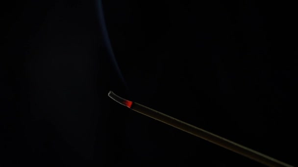 Крупный план горящей благовонной палочки. Дым дует с конца горячего угля. Запах, выпущенный из ладана на черном фоне. Расслабление, медитация и ароматерапия. 4k — стоковое видео