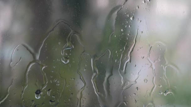 Silná dešťová voda se spláchne na okenní sklo a stéká dolů. Detailní záběr. Dešťové kapky na skleněném pozadí v období dešťů. 4k