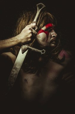 Etnik, yüz, uzun saç metal kılıç ve savaş boya ile vahşi savaşçı