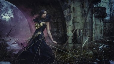 Altın ve siyah ipliklerden yapılmış gotik elbiseli güzel esmer kadın. Kışın karlı bir ormandadır. fantezi kavramı