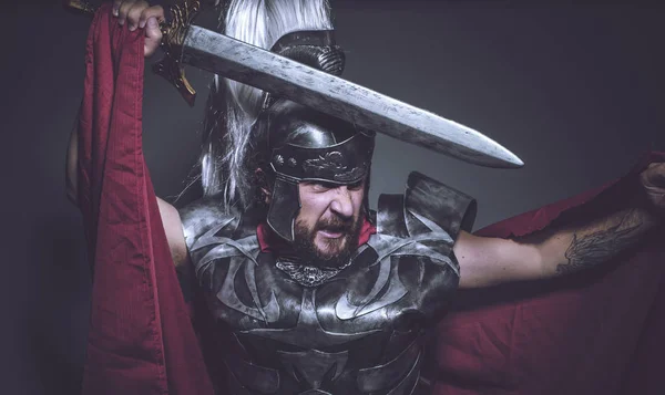 Roman gladiator, wrestler and warrior of Rome with helmet and red cloak, carries an iron sword, beard and long hair.