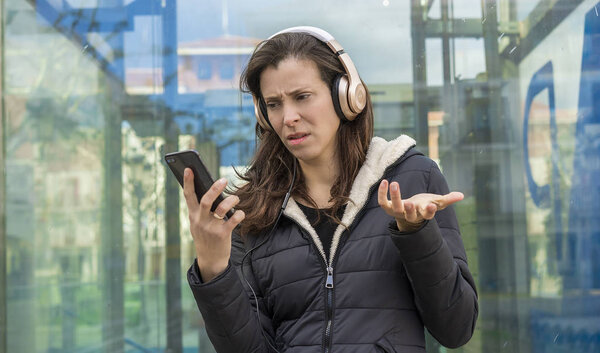 Отношения, ревность и подозрения в сотовом телефоне, пара проблем, взрослая женщина смотрит на подозрительные сообщения по телефону в то время как на улице слушать музыку с наушниками
