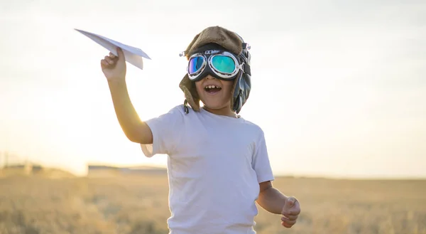 ヘルメットと日没で紙飛行機を再生しながらパイロットになる夢をはいた男の子 — ストック写真