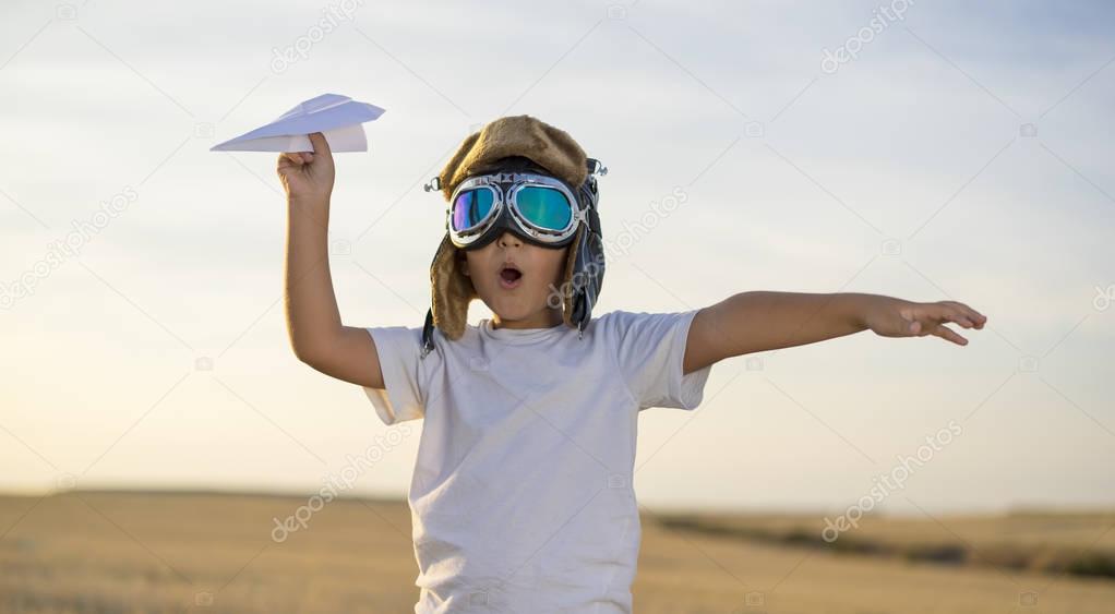 Little boy wearing helmet and dreams of becoming an aviator while playing a paper plane at sunset