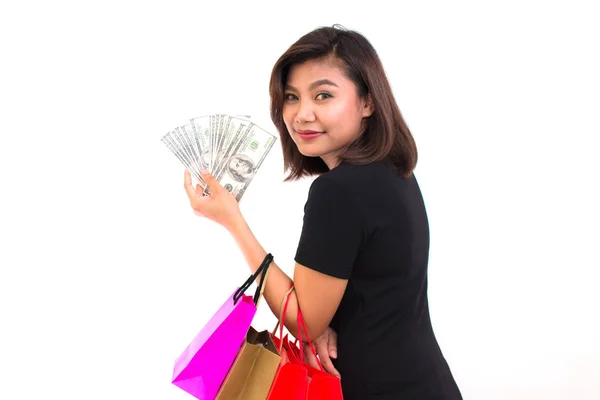 Mulher asiática nova bonita com sacos de compras coloridos. Uma mão detém dinheiro uma nota de cem dólares no fundo branco . — Fotografia de Stock