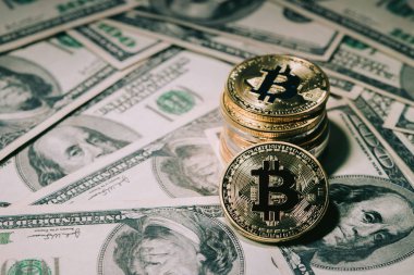 Yüz dolarlık banknotlar üzerinde yığın altın bitcoin yığını. Tek para bitcoin, iş yüzünde simgesi mektup B gölgelendirme ve kavram ticaret ile keskin odak kamera karşı karşıya.