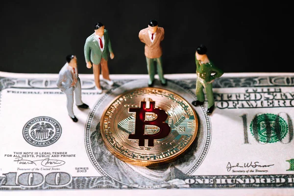 Miniaturowy ludzi małych figurek biznesmenów Stoiska i właśnie złoty bitcoin na sto Dolar banknotów. Elektronika pieniadze, cyfrowy obraz koncepcyjny Bitcoin, wydobycie i handel. — Zdjęcie stockowe