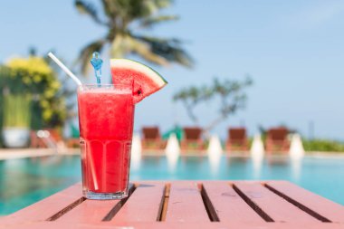 Sağlıklı kavramı, Yüzme Havuzu ve mavi gökyüzü arka plan ile ahşap bir masa üzerinde su kavun güler yüzlü.