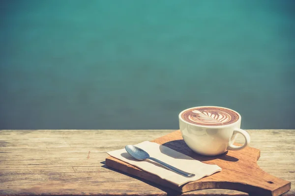 Винтаж искусства чашки горячего кофе капучино, ложки, ткани, доска для рубки на деревянном столе с копировальным пространством и речным фоном. позитивное мышление — стоковое фото