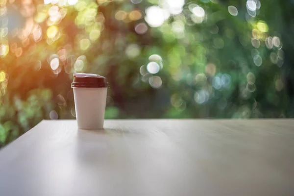 Размытая Одноразовая чашка кофе на деревянном столе над садовым пейзажем с солнечным светом. Красота природный фон, Боке природный фон. Чашка кофе на вынос . — стоковое фото