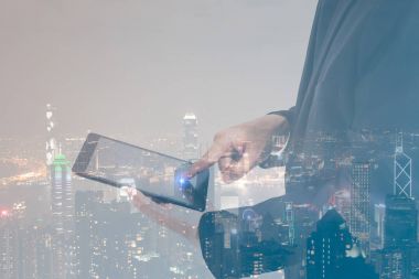 Siyah takım elbise ve modern şehir gece arka plan ile dijital tablet ile çalışan çift pozlama kavramı iş adamı. Boş ekran işiniz için hazır.