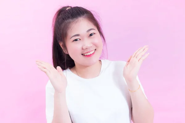 Retrato da bela jovem asiática cabelo preto usar uma camiseta branca com a mão aberta. Sentimento feliz e brilhante. Menina linda linda olhando para a câmera com sorriso adorável. isolado em fundo rosa . — Fotografia de Stock