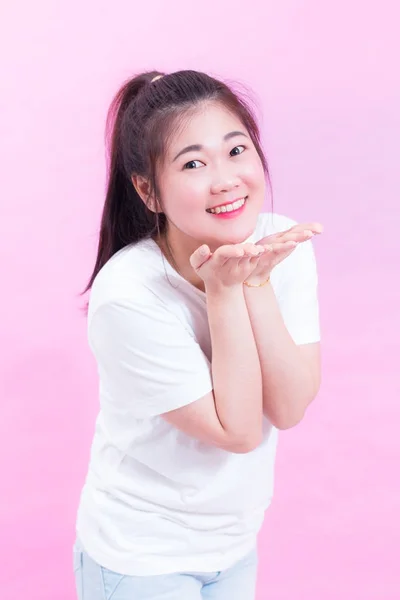 Bonito lindo de bela jovem asiática cabelo preto usar uma t-shirt branca de pé e enviar beijo sobre fundo rosa. Mulher asiática soprando beijo e olhando para a câmera . — Fotografia de Stock