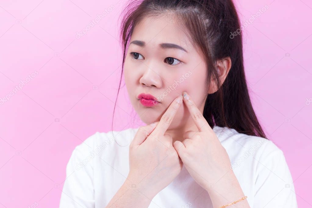 Portrait of beautiful Young Asian woman black hair wear a white t-shirt squeezing pimples on her face. Checks her skin, Skin care, Acne treatment, Problem with acne. isolated on pink background.