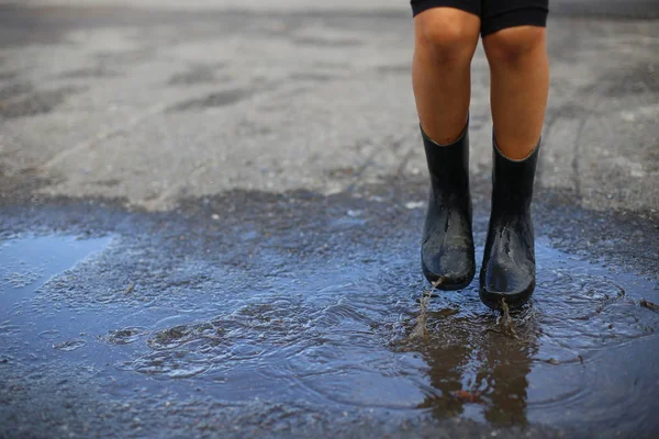 child with rain boots jumps into a puddle