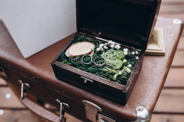 Altın alyanslar iplerin üzerinde, tahta bir kutunun içinde, çimlerin üzerinde duran bir ayna ile duruyor..